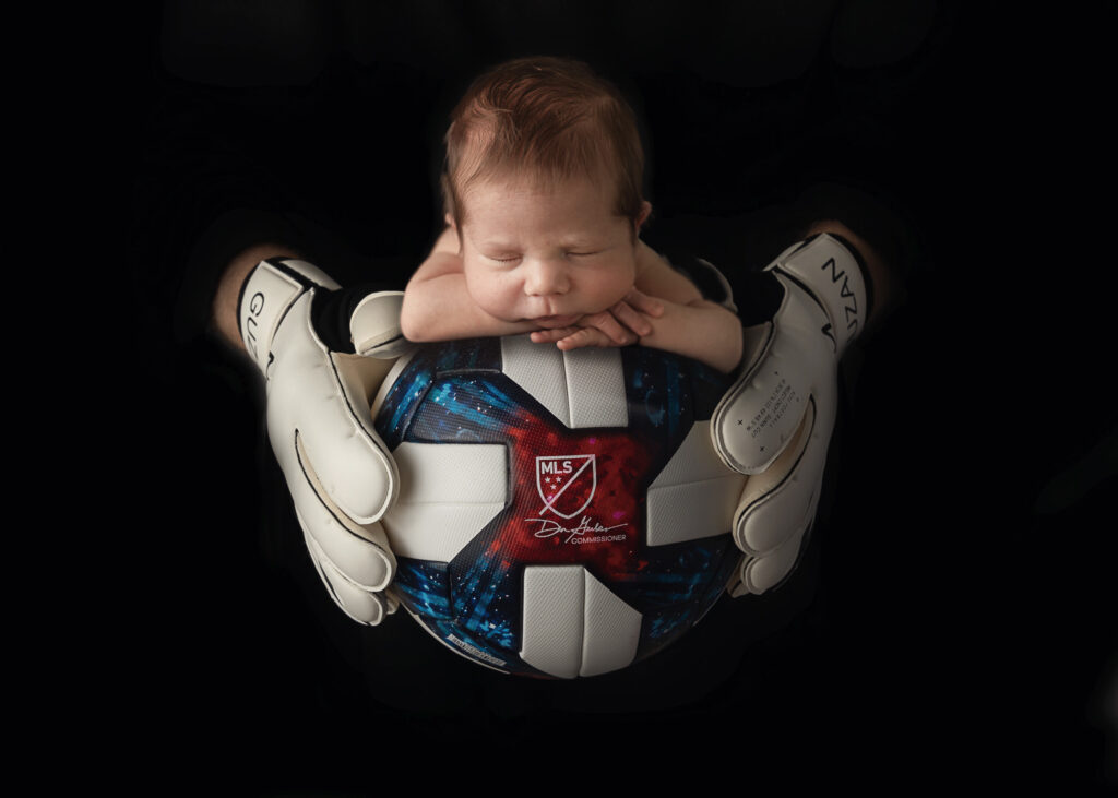 baby boy photographed on a soccer ball with dad Brad Guzan holding it