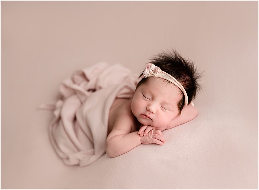 baby girl, laying down with pink backdrop and pink wrap