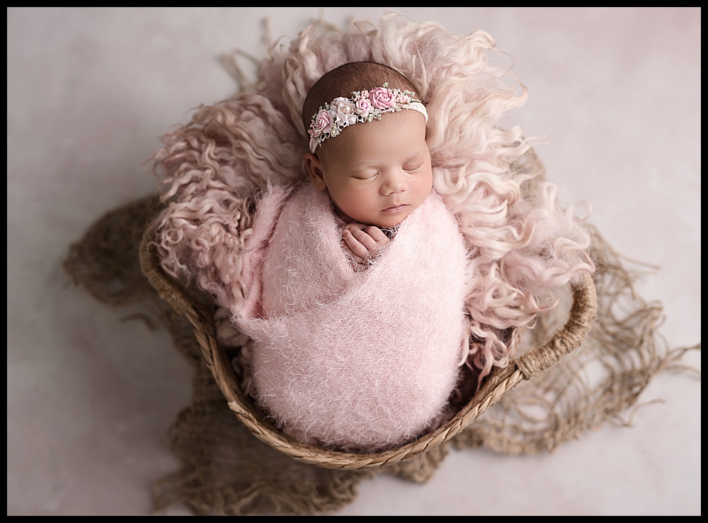 baby girl wrapped in pink, laying in a basket