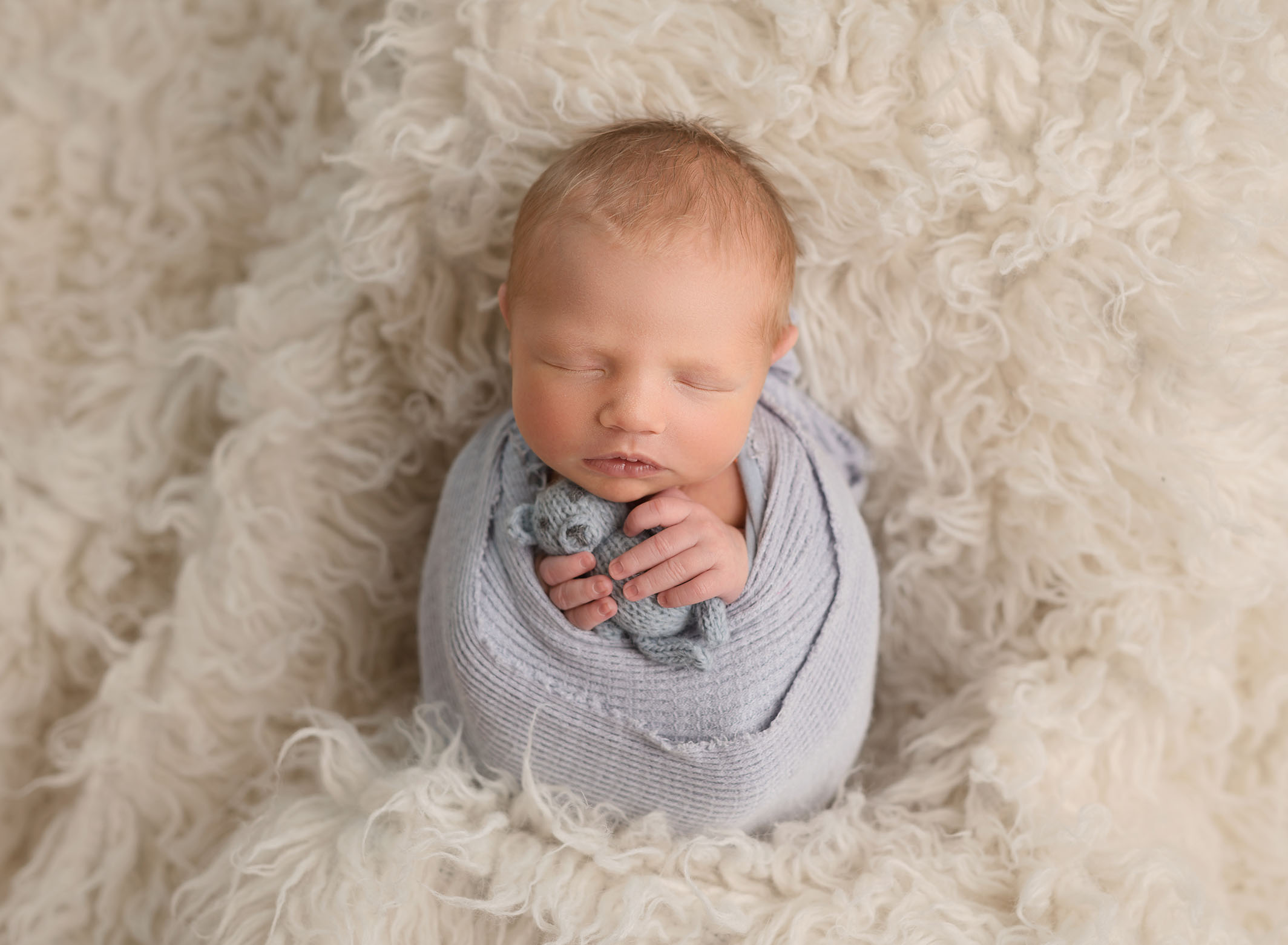 baby boy wrapped in light blue laying on cream color rug