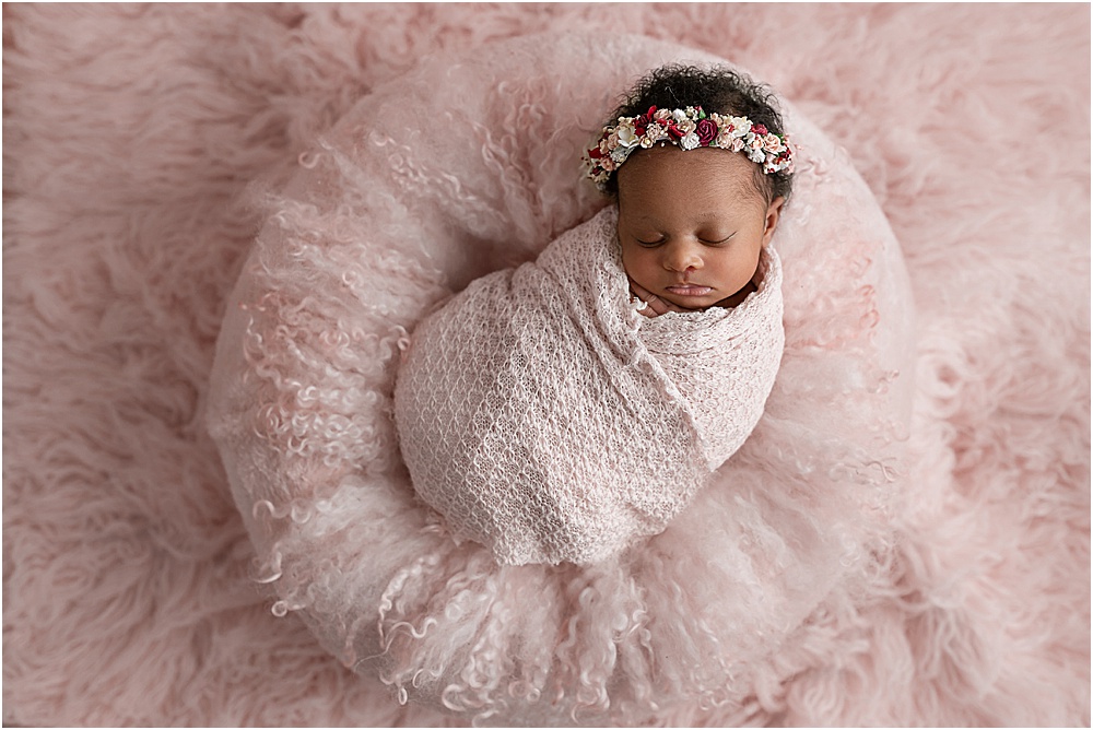 baby girl laying on a pink pillow and swaddle