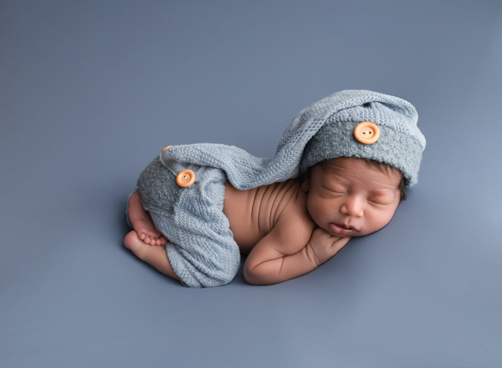 baby boy laying on blue background wearing pants and sleepy hat